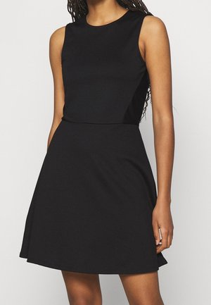 Robe noire sans manches avec une taille cintrée et une jupe évasée portée par une personne aux cheveux lâches et tressés.