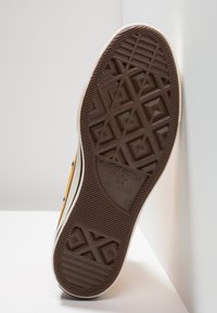 Rjava gumijasta podloga za teniske copate z teksturiranim geometrijskim vzorcem, ki vključuje stransko črto in blagovno znamko 'Converse All Star'.