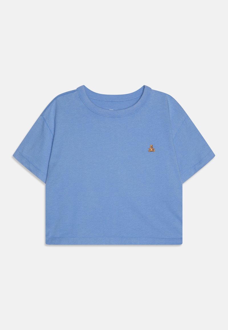 T-shirt cropped bleu en tissu doux, avec des manches courtes et un col rond. Comprend un petit accent brodé sur la poitrine.