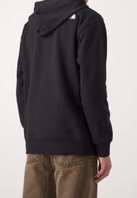 Felpa nera con cappuccio dalla vestibilità comoda, con polsini e orlo a costine e un piccolo logo bianco sulla spalla posteriore.