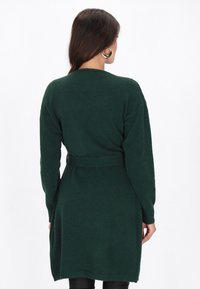 Grüne Strickjacke mit langen Ärmeln, einem Taillengürtel und einer lockeren Passform. Weiche Textur, mittellange Schnittführung und minimalistische Details.