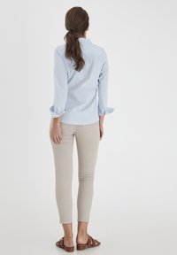 Jasnoniebieska koszula z długim rękawem z podwiniętymi rękawami, w połączeniu z beżowymi wąskimi spodniami i brązowymi sandałami, widziana z tyłu.