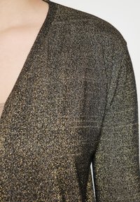 Cardigan metallizzato a maglia con scollatura a V profonda, in nero con fili dorati, che mette in evidenza una superficie testurizzata e luccicosa.
