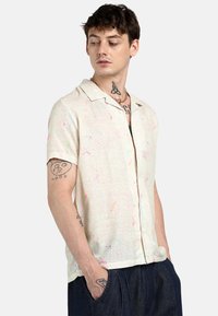 Camicia a maniche corte con bottoni in tessuto cremoso testurizzato, caratterizzata da motivi astratti multicolore. Presenta un colletto a punte e una vestibilità rilassata.