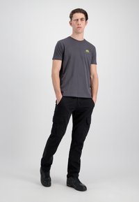 Grå crew-neck t-shirt med et lille grønt logo, parret med sorte cargo-bukser med flere lommer og en afslappet pasform.