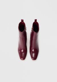Bottines en cuir bourgogne avec un bout pointu, texture lisse et une fermeture éclair sur le côté. Elles disposent d'une languette de tirage pour un enfiler facile.