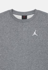 Pilkas džemperis, pagamintas iš medvilnės mišinio. Turi apvalią kaklo išpjovą, minkštą tekstūrą ir baltą išsiuvinėtą Jumpman logotipą krūtinėje.