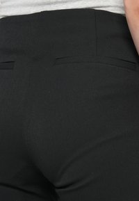 Black tailored trousers featuring a smooth fabric, subtle sheen, and two back pockets. The fit is structured and designed for a polished appearance.