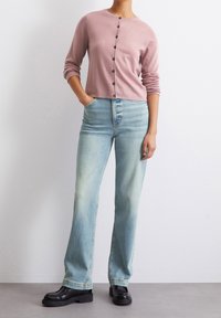 Cardigan rose à boutons avec un col rond, associé à un jean évasé bleu clair et des chaussures à plateforme noires. La tenue présente une coupe décontractée.