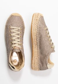 Baskets en textile beige avec une texture tissée, bout rond et lacets légers. Présentent une semelle enroulée de jute et des accents métalliques sur les semelles intérieures.