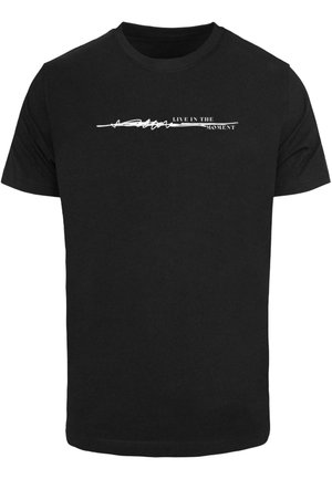 Černé bavlněné tričko s bílým grafickým textem, který horizontálně přes hruď zní "ŽIJTE V SOUČASNOSTI". Klasický design s kulatým výstřihem.