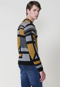 Suéter de punto con patrones geométricos en amarillo, gris y negro. Mangas y dobladillo de ribetes, con un corte regular y escote redondo.
