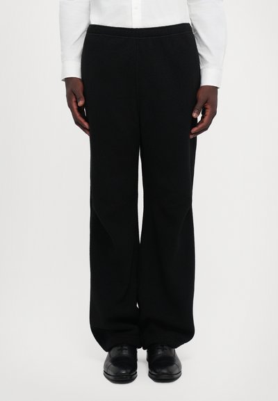 Pantaloni in pile neri con vestibilità comoda, vita elasticizzata e gambe ampie. Presentano un tessuto testurizzato e nessun motivo o hardware visibile.