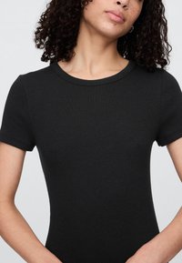 Czarny prążkowany krótki top z okrągłym dekoltem i dopasowanym krojem, podkreślający gładką fakturę i minimalistyczny styl.