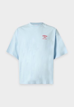 Svetlomodré tričko s krátkym rukávom s červeným logom "Adidas Since 1972" na ľavej strane hrude, zobrazené na jednoduchom pozadí.