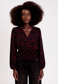 Czarna bluzka z nadrukiem czerwonej róży i serca, z dekoltem w serek, długimi bufkami i marszczonym pasem. W połączeniu z ciemnymi, prostymi dżinsami.