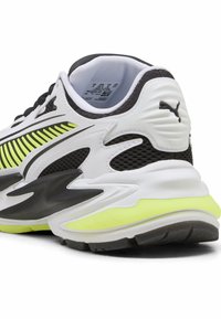Schwarz-weißer Sportschuh mit einem Mesh-Obermaterial, neon-gelben Akzenten, strukturierten Seiten und einem klobigen Sohlen-Design.