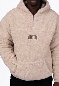 Beige fleece pullover with a half-zip, featuring a front pocket and “CRYSTAL” embroidered in brown. Soft, textured surface detail.