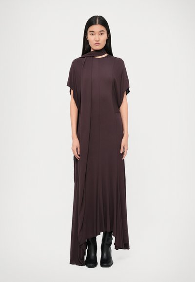 Robes longues et fluides de couleur marron en tissu doux, avec des manches larges et un design drapé à encolure haute. Porté avec des bottes noires.