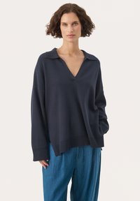 Diepblauwe pullover trui met V-hals en puntige kraag. Heeft een losse pasvorm en geribbelde details bij de mouwen en de zoom. G styling met lichtblauwe broek.