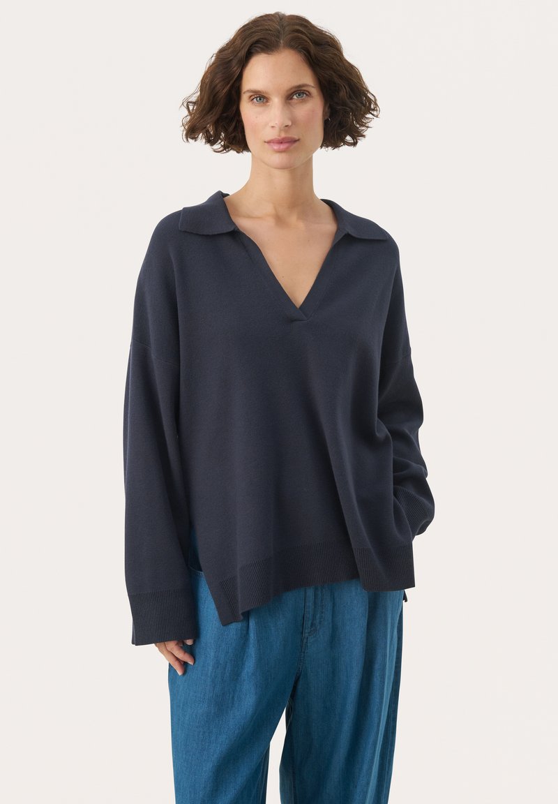Diepblauwe pullover trui met V-hals en puntige kraag. Heeft een losse pasvorm en geribbelde details bij de mouwen en de zoom. G styling met lichtblauwe broek.