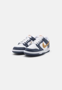 Balti ir tamsiai mėlyni sportbačiai su tekstūruoto odos viršumi, perforuota pirštų dėžute, auksiniu Swoosh logotipu ir baltais raišteliais. Guma pado lauko sluoksnis užtikrina sukibimą.