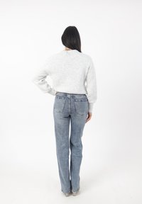 Ljusgrå ribbad tröja med långa ärmar, matchad med högmidjade blå jeans med raka ben och två bakfickor.
