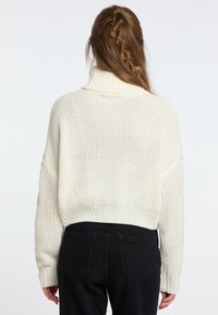 Cremfarbener gestrickter Pullover mit hohem, geripptem Kragen und überschnittenen Schultern. Verfügt über ein strukturiertes Muster und eine verkürzte Länge.