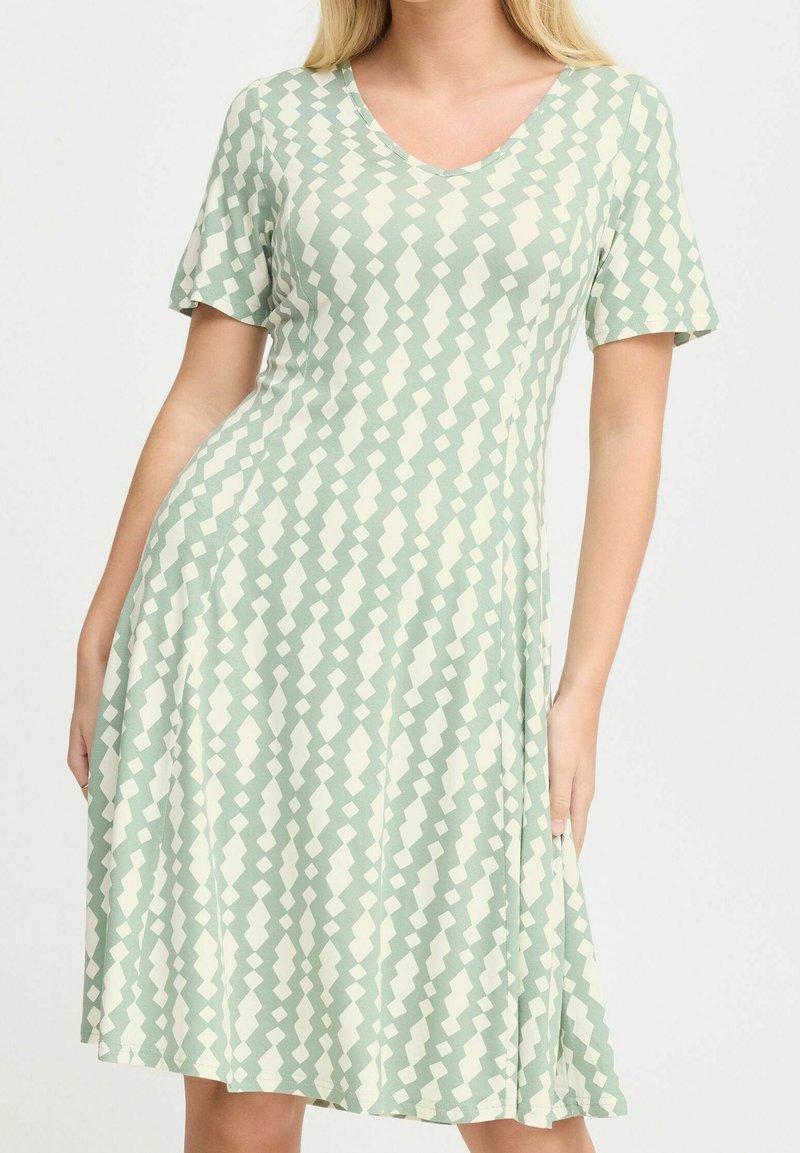 Femme portant une robe à manches courtes, longueur genoux, avec un motif géométrique vert clair et blanc.