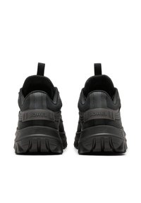 Musta urheilukenkä, jossa on teksturoitu kangaspäällinen, kumipohjat ja vetolenkit kantapäällä; ominaisuuksiin kuuluu kohotettu logo ja kontrastiväriset yksityiskohdat.