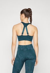 Sutiã desportivo teal com alças ajustáveis e um design racerback, combinado com leggings de cintura alta num padrão coordenado. Tecido liso e elástico.