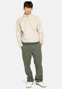 Jasno beżowy polar z zamkiem błyskawicznym do połowy, ozdobiony małym logo, w połączeniu z luźnymi zielonymi spodniami cargo z przednimi kieszeniami i swobodnym krojem.