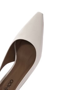Białe skórzane szpilki z zaostrzonym noskiem i otwartym wycięciem po bokach oraz brązową wkładką. Gładka faktura, elegancki design i minimalne dodatki.