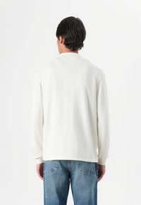 Weißes Langarmshirt mit Rundhalsausschnitt und gerippten Bündchen, kombiniert mit hellblauen Jeans. Strukturiertes Material mit lockerer Passform.