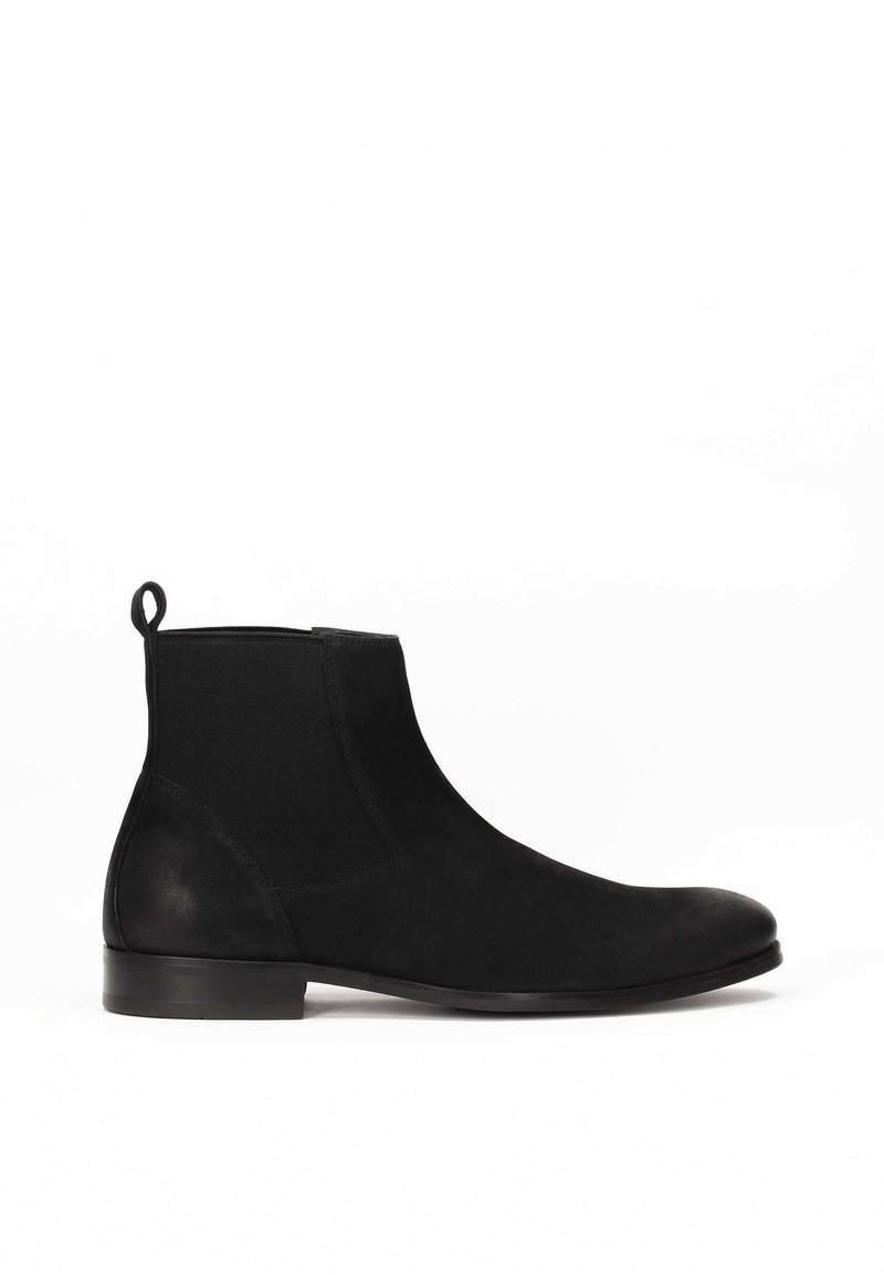 Botas Chelsea negras de ante con paneles laterales elásticos, textura suave, punta redondeada y una pestaña en el talón. Suela de goma plana.