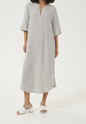 Robe légère à rayures avec décolleté en V et manches trois-quarts. Couleur : blanc avec rayures foncées. Associée à des chaussures blanches à talons blocs ouverts à l'avant.