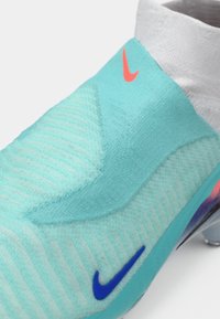 Cizma de fotbal texturată de culoare albastru deschis, cu o suprafață nervurată. Dispune de un tiv alb, un logo Nike albastru și un mic accent portocaliu. Talpă transparentă.