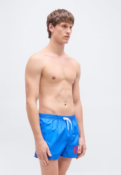 Μπλε μαγιό σορτς από απαλό, ελαφρύ υλικό με ελαστική μέση και λευκό κορδόνι. Διακοσμείται με ένα μεγάλο κόκκινο γράμμα "D" στο μπροστινό μέρος.