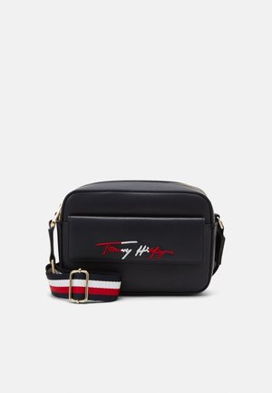 Sac bandoulière rectangulaire noir avec poche avant, bandoulière réglable rouge, blanche et bleue, et logo signature rouge et blanc sur la poche.