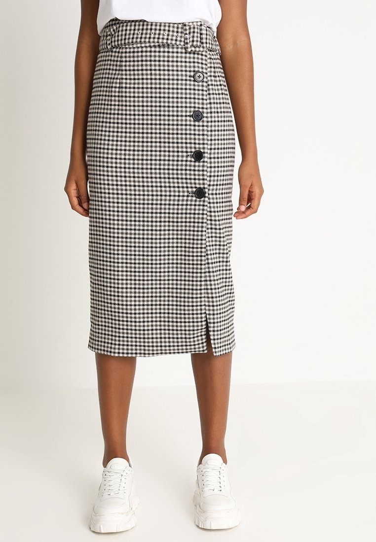 Falda midi de cuadros en blanco y negro con corte recto, que presenta una abertura frontal y cinco botones negros a lo largo del costado. Combinada con zapatillas blancas.