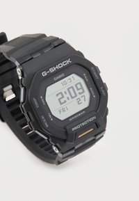Reloj G-Shock negro con pantalla digital; presenta una correa texturizada, una esfera hexagonal y una carcasa protectora. Resistente al agua hasta 20 bar.