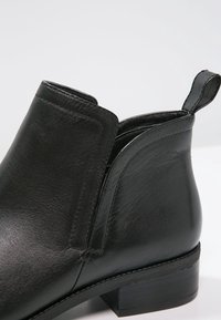 Bottine en cuir noir avec un petit talon empilé et une languette à l'arrière, présentée en gros plan sur fond blanc.