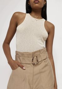 Beige ribbed tílko s kulatým výstřihem v kombinaci s béžovými kalhotami s vysokým pasem, které mají široký opasek a detail čtverkové spony.