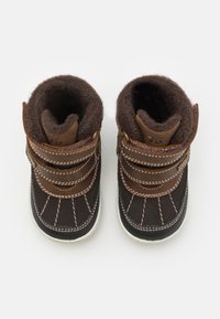 Brune støvler med mykt pelsfôr, som har to justerbare stropper, kontrasterende brune lærdetaljer og en hvit gummisåle.