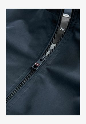 Tessuto di giacca nero con una texture liscia. Presenta una chiusura frontale con cerniera dotata di una robusta linguetta e sottili linee decorative rosse e bianche.