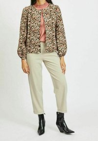 Blommönstrad jacka i nyanser av brunt och kräm, med puffärmar, ihop med en rosa blus och ljusa beigefärgade byxor, avslutad med svarta ankelboots.