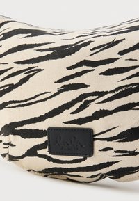 Καμβά τσάντα με μπεζ φόντο και μοτίβο μαύρων ρίγων τίγρης. Διαθέτει μαύρη δερμάτινη ετικέτα με την επωνυμία "lala BERLIN." Επιπεδωμένο σχήμα.