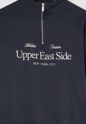 Pullover blu navy con colletto alto e zip a quarto. Presenta testo ricamato bianco: "Upper East Side, New York City" e "Athletic Season."