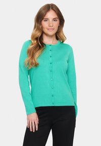 Mündroheline kootud kardigan pika varrukaga, ümmarguse kaelusega ja nööbiga kinnitusega. Omab ribakujundust ja vormitud disaini.