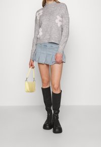 Maglione grigio a maglia con motivi floreali rosa, mini gonna in denim plissettata blu chiaro, borsa gialla in faux crocodile e stivali neri alti fino al ginocchio con tacco.